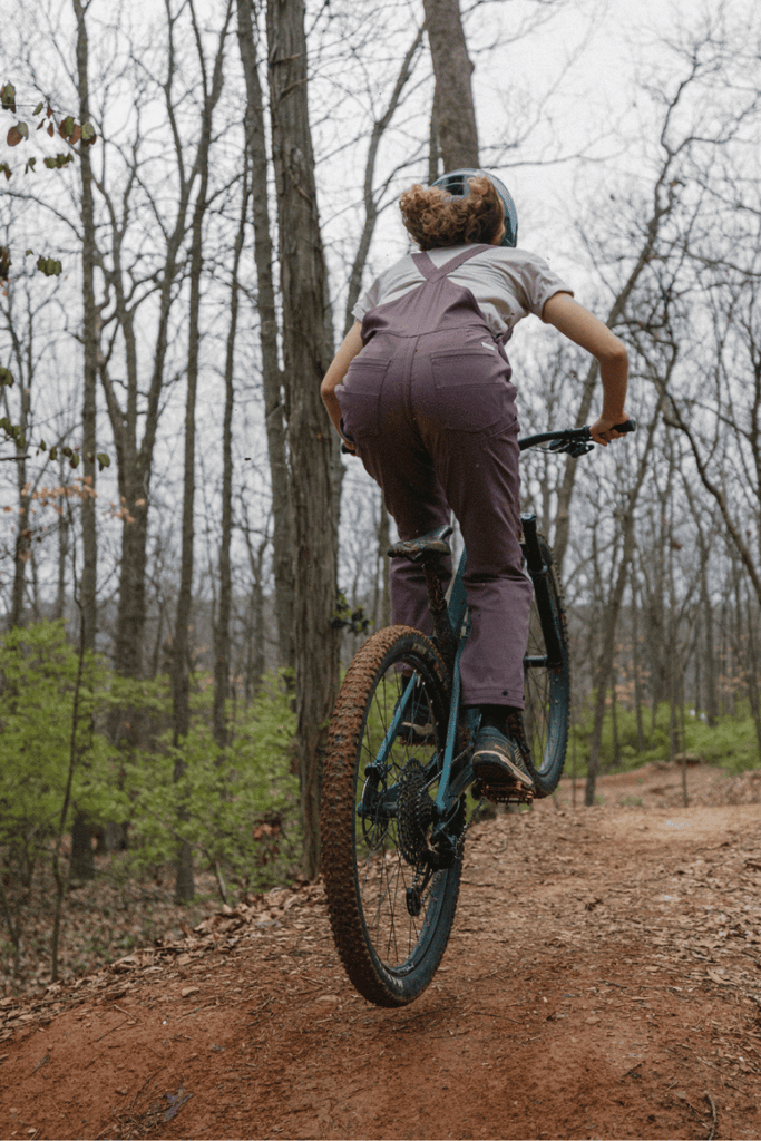 Lifestyle photo of model on bike in Ecotrek overalls in Plum