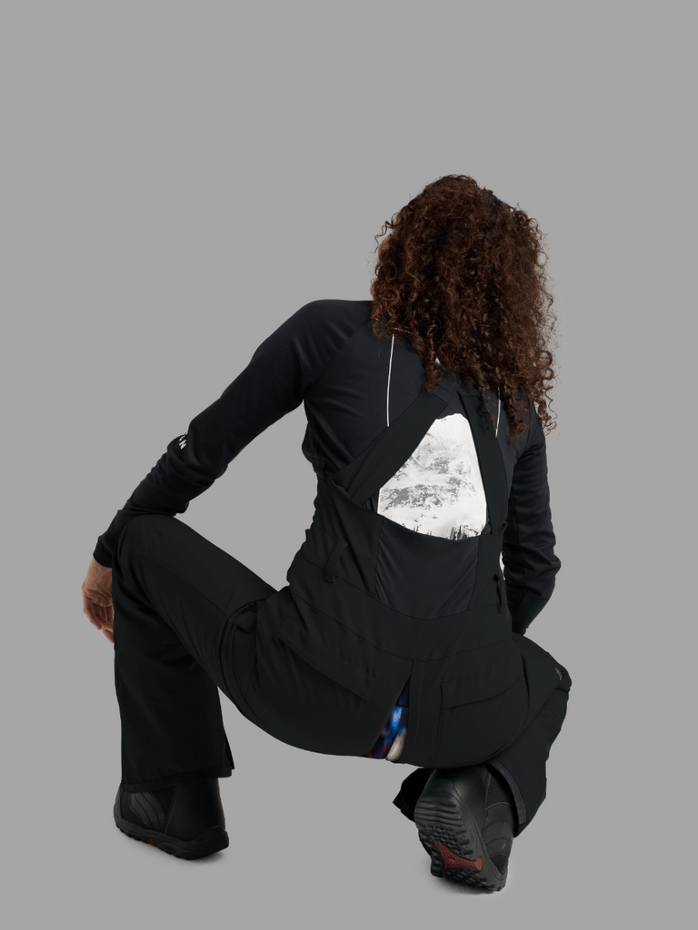 Model in squatting pose facing the back with GoFly zipper exposed to base layer in Burton Bib in Black.
