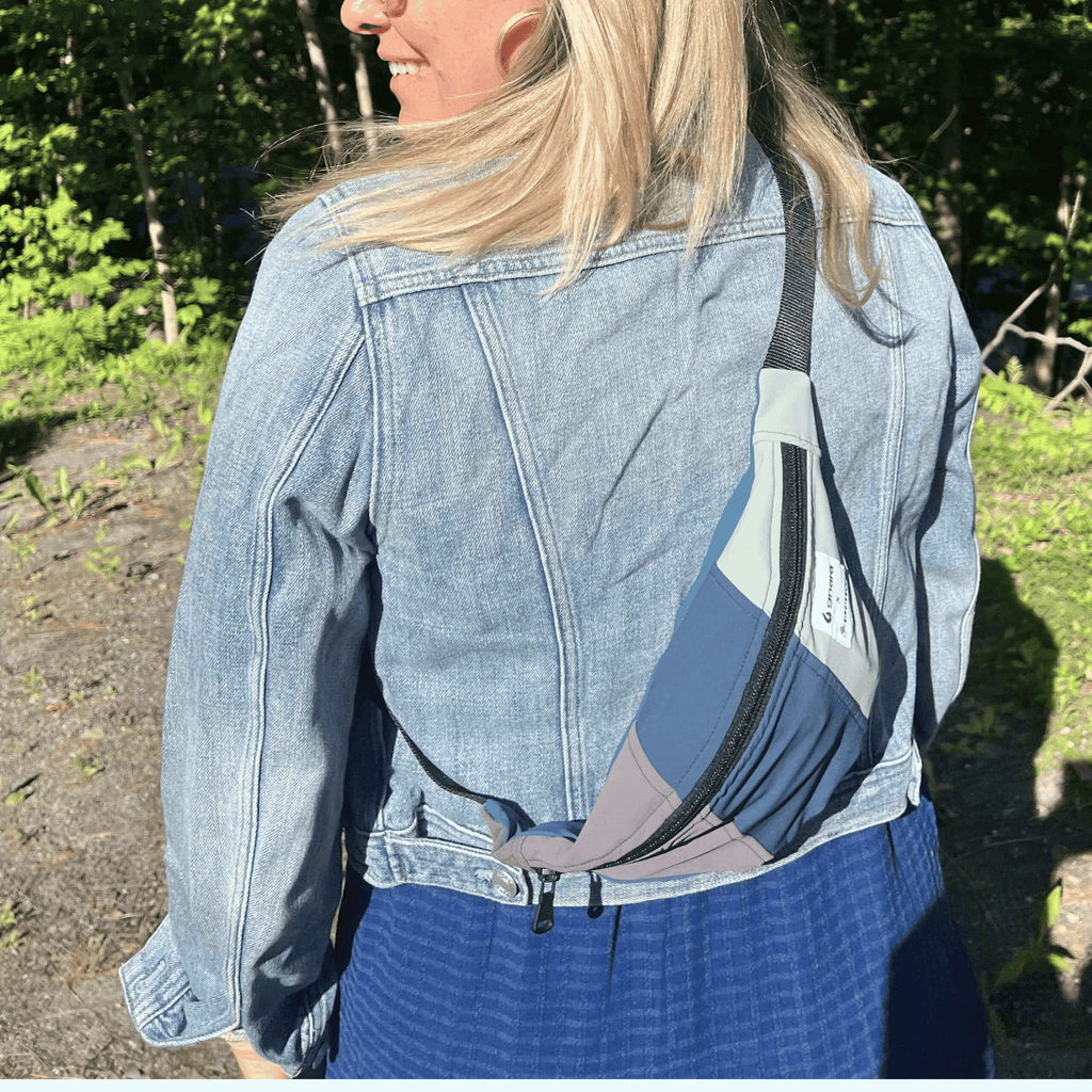 Person wearing a denim jacket with fanny pack over one shoulder outdoors.